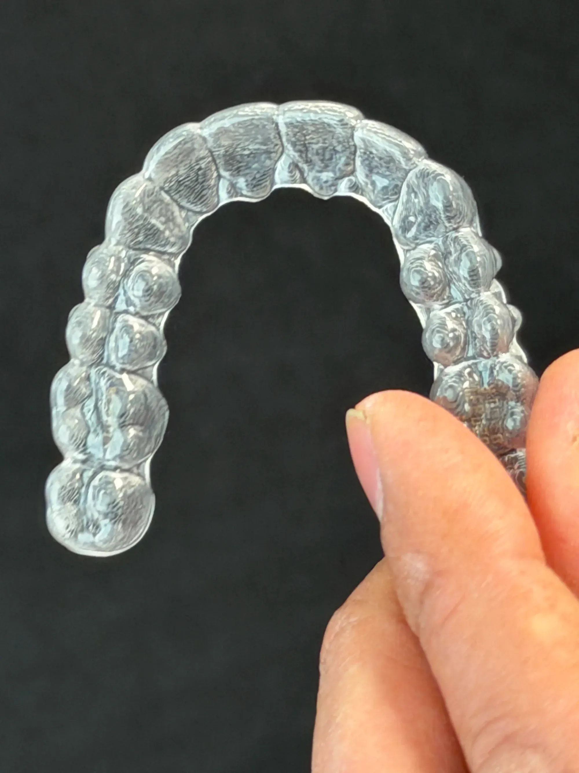 Nærbilde av en gjennomsiktig Invisalign-skinne holdt mellom to fingre